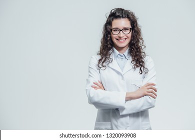 Portrait of smiling young female doctor. Beautiful brunette in white medical gown in glasses. Holding without a stethoscope on a gray background.