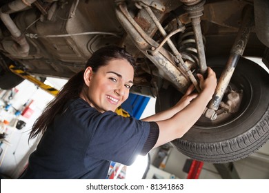 Portrait of smiling young female mechanic inspecting a CV joing on a car in auto repair shop - Powered by Shutterstock