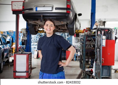 Portrait Of Smiling Young Female Mechanic With Hands On Hips In Auto Repair Shop