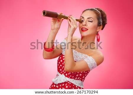 Portrait of a smiling young female model with hand-held telescope in her arms wearing red dress