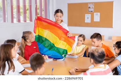 Portrait of smiling young female teacher conducting lesson for tweens, talking about LGBT community and showing rainbow flag - Powered by Shutterstock