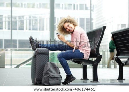 Portrait of smiling young female traveler waiting with bag and cellphone
