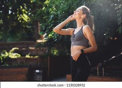 Portrait of a smiling young fitness girl listening to music through wireless earphones outdoors