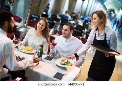 Portrait of smiling young friends in outdoors restaurant and smiling waitress