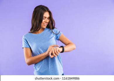 Portrait of a smiling young girl looking at her smartwatch isolated over violet background - Powered by Shutterstock