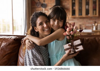 Portrait Of Smiling Young Hispanic Mother And Little Daughter Hug Cuddle Show Love And Care. Happy Latino Mom And Small 8s Girl Child Embrace At Home, Feel Grateful Thankful. Family Bonding Concept.