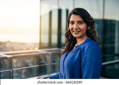 Portrait Of A Smiling Young Indian Businesswoman Standing Outside On An Office Building Balcony Overlooking The City At Dusk