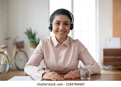 Portrait Of Smiling Young Indian Female Employee In Headphones Look At Camera Talk On Video Call With Client. Happy Ethnic Woman Worker In Headset Have Webcam Digital Virtual Consultation On