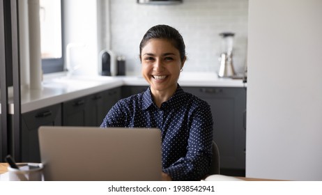 Portrait Of Smiling Young Indian Woman Sit At Desk In Home Office Work On Laptop Online. Happy Mixed Race Ethnicity Female Employee Use Computer Consult Client Customer On Web. Technology Concept.