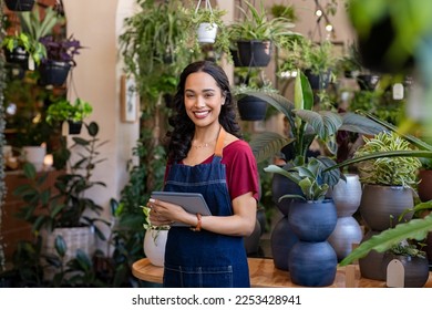 Portrait of smiling young latin woman florist standing and holding digital tablet at floral shop. Successful flower shop owner standing in plant store looking at camera. Happy mixed race entrepreneur. - Powered by Shutterstock