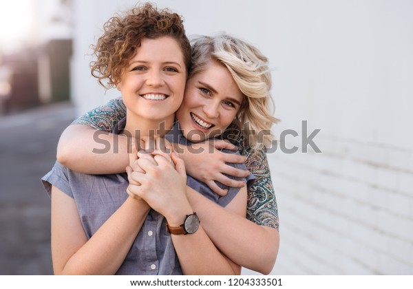 都会の通りに立ち お互いに抱き合いながら微笑む若いレズビアンのカップルのポートレート の写真素材 今すぐ編集
