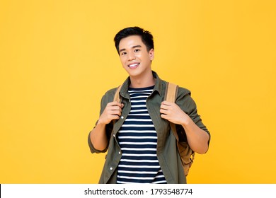 Portrait Of Smiling Young Male Asian Tourist Carrying Backpack Ready To Travel In Isolated Studio Yellow Background