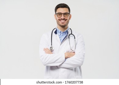Portrait of smiling young male doctor with stethoscope around neck standing with crossed arms in white coat, isolated on gray background 
