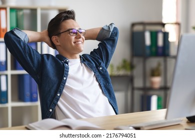 Portrait Of Smiling Young Male Entrepreneur Relaxing At Workplace In Office, Happy Millennial Businessman Leaning Back In Chair With Hands Behind Head, Resting At Desk After Working With Laptop