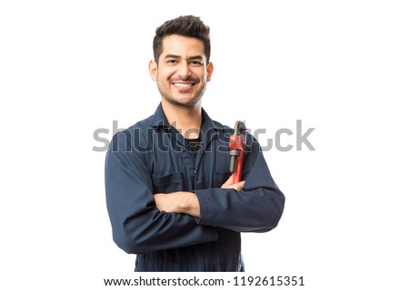 Portrait of smiling young male plumber with pipe wrench standing arms crossed on white background