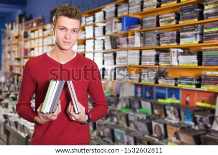 Portrait of smiling young male with stack of DVDs in hands in store  