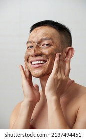 Portrait Of Smiling Young Man Applying Face Scrub To Exfoliate Skin