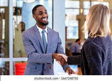 Portrait Of A Smiling Young Man In Business Suit With Female Client Or Business Woman  Shaking Hands In Office Meeting 