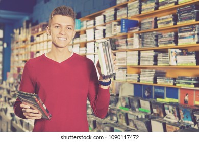 Portrait of smiling young man with stack of DVDs in hands in store  