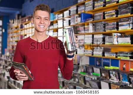 Portrait of smiling young man with stack of DVDs in hands in store  