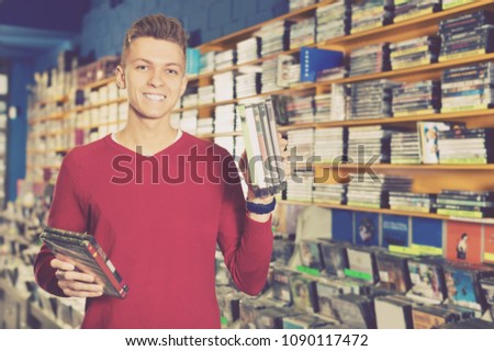 Portrait of smiling young man with stack of DVDs in hands in store  