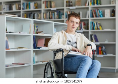 Portrait of smiling young man using wheelchair in school library and looking at camera, copy space - Powered by Shutterstock