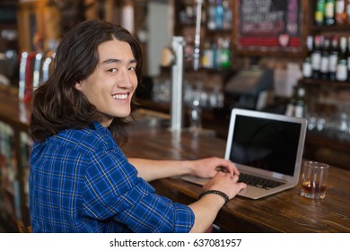 Portrait of smiling young man using laptop at bar counter