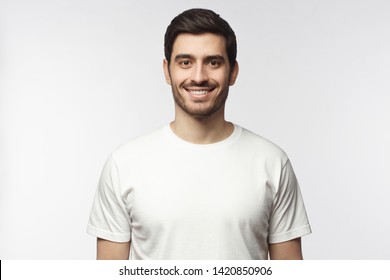 Portrait Of Smiling Young Man In White T-shirt Looking At Camera, Isolated On Gray Background