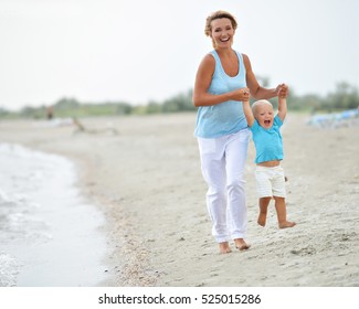 Portrait Of Smiling Young Mother With Little Child Running On The Beach.