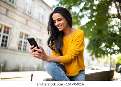 Portrait Smiling Young North African Beautiful Woman Sitting Outside In City Looking At Mobile Phone