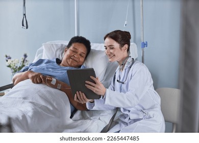 Portrait of smiling young nurse showing digital tablet screen to senior African American woman in hospital bed - Powered by Shutterstock