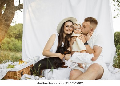 Portrait Of Smiling Young Parents Embarrassing Their Little Daughter And Dog With Delicious Birthday Cake. Happy Family Of Three Having Birthday Party On Fresh Air.