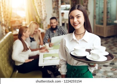 Portrait smiling young waitress standing in cafe. The happy girl the waiter holds in bunches a tray with utensils. Spacing orders to visitors of the restaurant. Restaurant service.