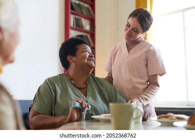Portrait of smiling young woman assisting female patient during dinner at nursing home, copy space