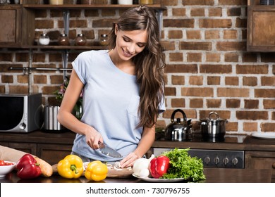 Portrait Of Smiling Young Woman Cutting Mushrooms While Cooking Dinner At Home