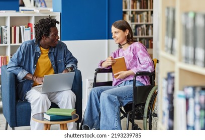 Portrait Of Smiling Young Woman With Disability Talking To Friend While Studying Together In Library