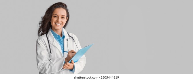 Portrait of smiling young woman doctor in uniform holding clipboard, looking and smiling at camera, friendly therapist woman with stethoscope posing on grey wall background, copy space - Powered by Shutterstock