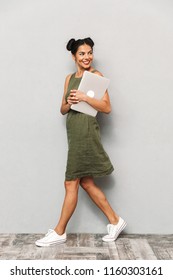 Portrait Of A Smiling Young Woman In Dress Isolated, Carrying Laptop Computer, Walking