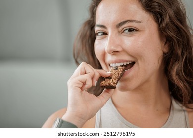 Portrait of a smiling young woman eating a protein bar with chocolate chips. Close up, copy space. - Powered by Shutterstock