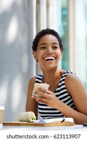 Portrait Of Smiling Young Woman Eating Sandwich Outside