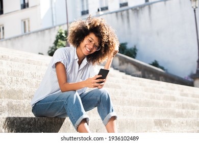 Portrait Smiling Young Woman With Eyeglasses Sitting Outside Looking At Phone