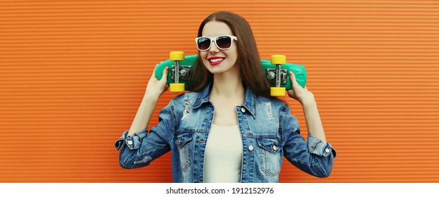 Portrait of smiling young woman with green skateboard on a colorful orange background