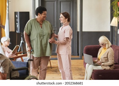 Portrait of smiling young woman helping seniors in modern retirement home, copy space
