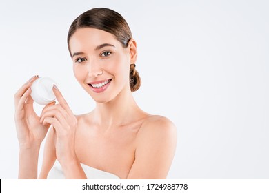 Porträt einer lächelnden jungen Frau, die eine Creme hält, die sich isoliert über weißem Hintergrund posiert