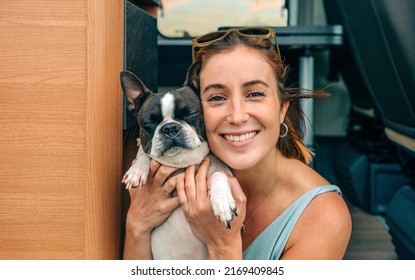 Portrait Of Smiling Young Woman Hugging Her Boston Terrier Dog In Front Of Camper Van