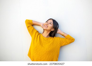 Portrait smiling young woman leaning against white wall with hands behind head - Powered by Shutterstock