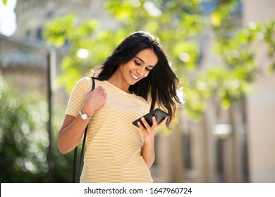 Portrait Of Smiling Young Woman Looking At Mobile Phone Outside In City