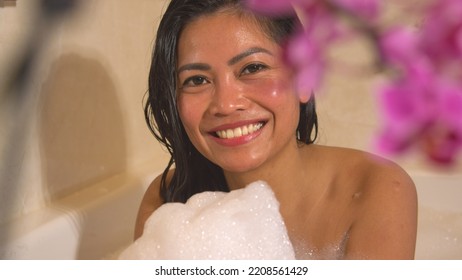 PORTRAIT: Smiling Young Woman Looking Into Camera With Hands Full Of Bath Foam. Female Person Laughing And Enjoying In Bathtub Full Of Bubble Foam. Home Relaxation In Bubbly Bath After A Long Busy Day