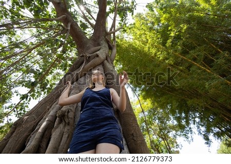 Portrait of smiling young woman at a park on a beautiful sunny day.  Woman with open arms in front of a big a tree. Green and nature background. High quality photo