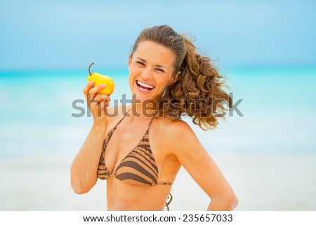 Portrait of smiling young woman with pear on beach
